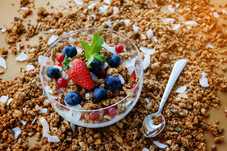 a glass bowl of granola, berries and mint with a spoon