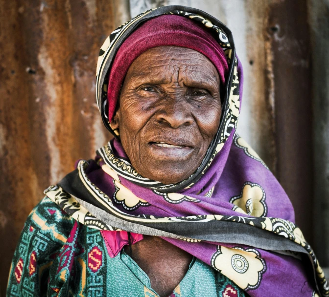 a woman standing next to a rusty fence wearing a scarf