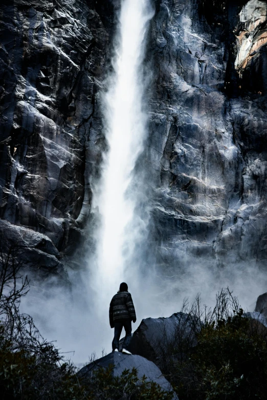 a man sits looking at a waterfall