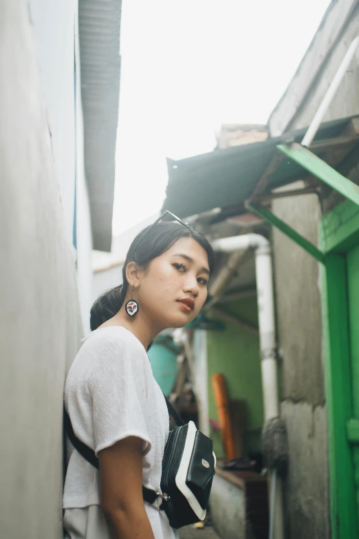 a woman wearing earrings stands near the wall