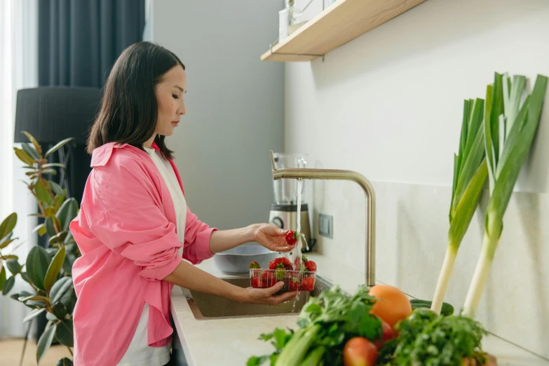 woman in kitchen adding strawberries to fruit