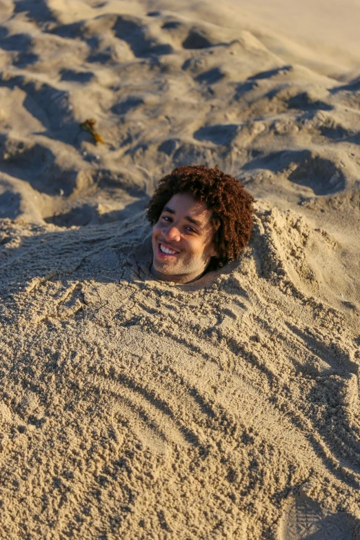 smiling man laying in the sand and buried in sand