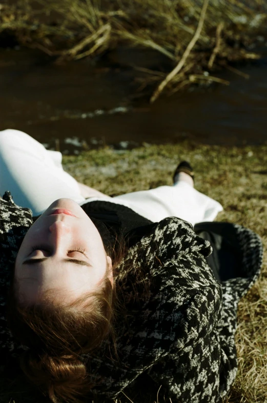 the person is laying down on the grass near a river