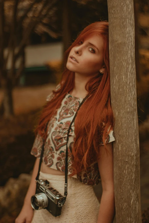 a young redhead woman holds a camera in her left hand and looks up