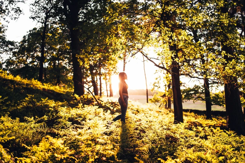 a woman standing on a grassy hill surrounded by trees