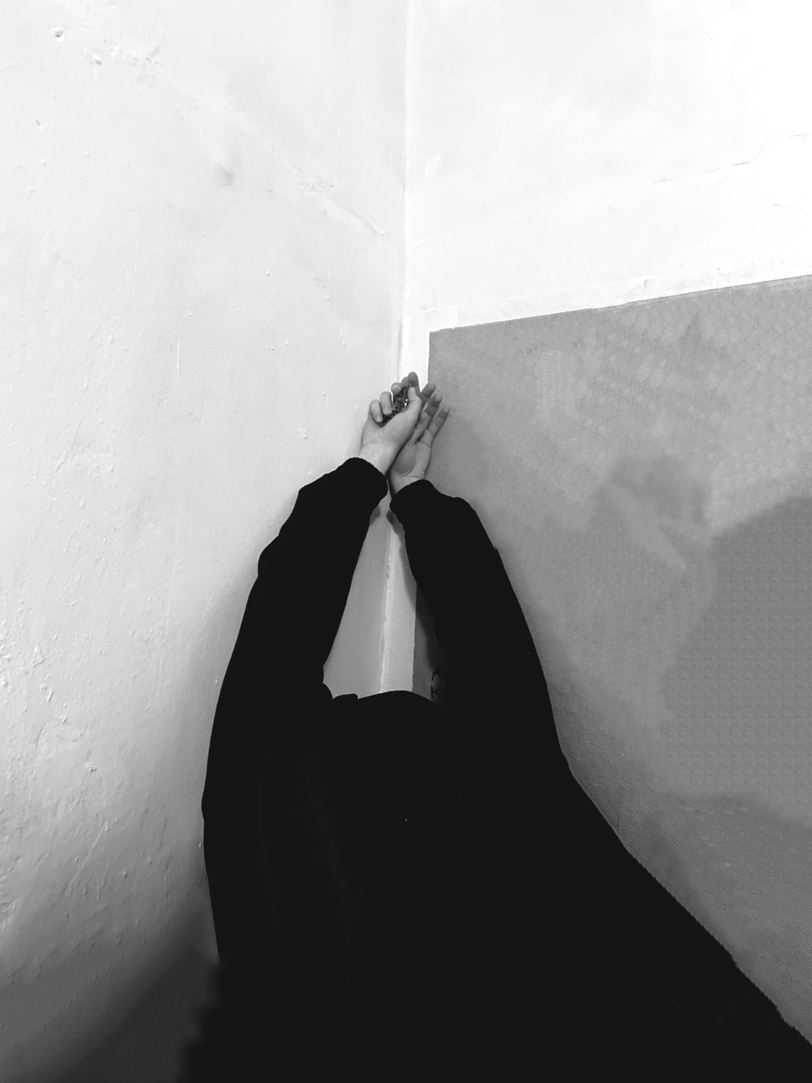 a person with a long black jacket on is holding his hand against the wall