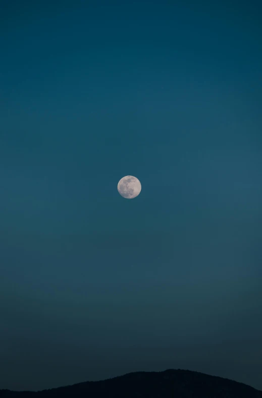 the full moon setting behind the mountains on a clear day