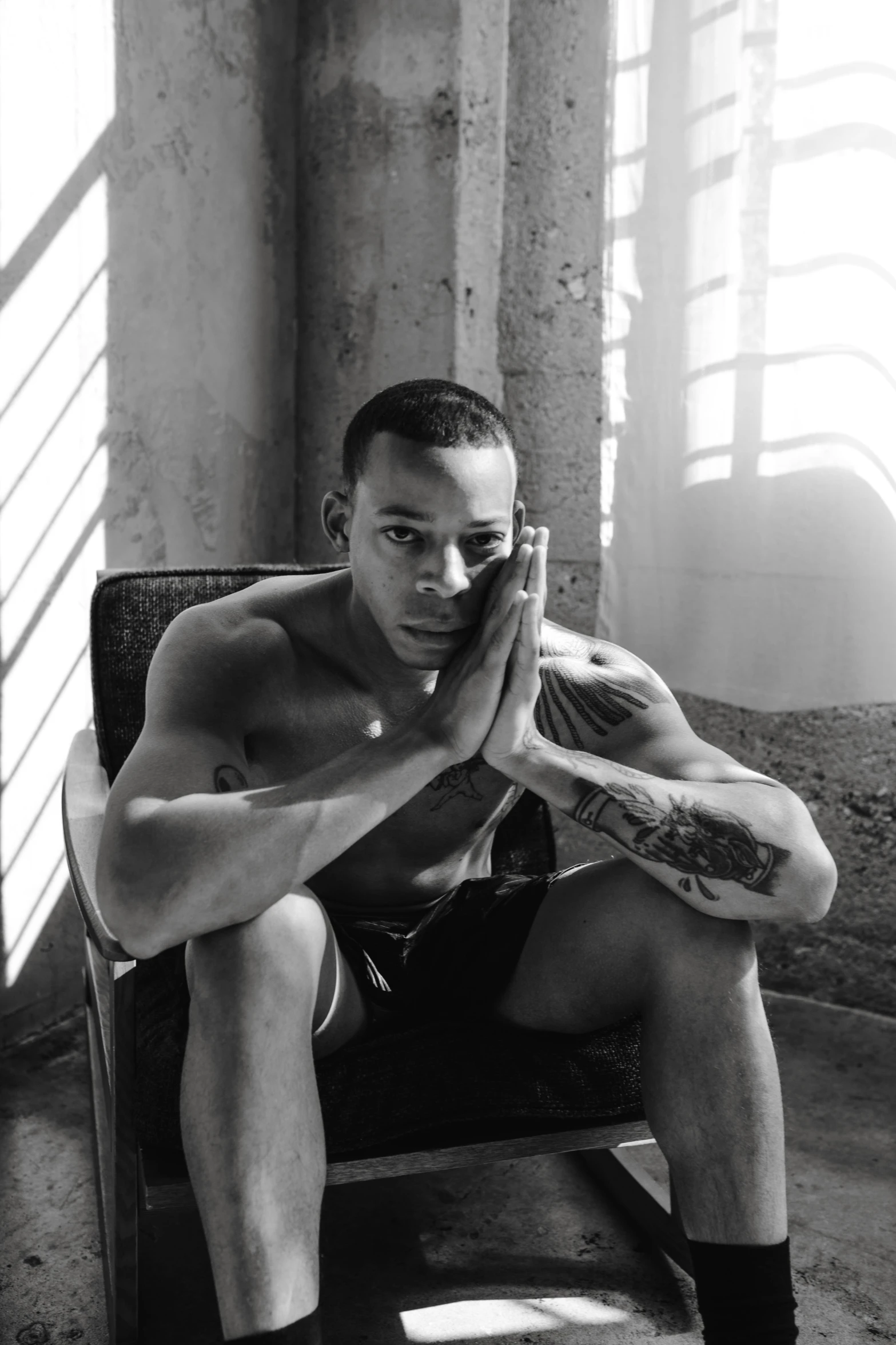 shirtless man with tattooed arms sits in an industrial chair