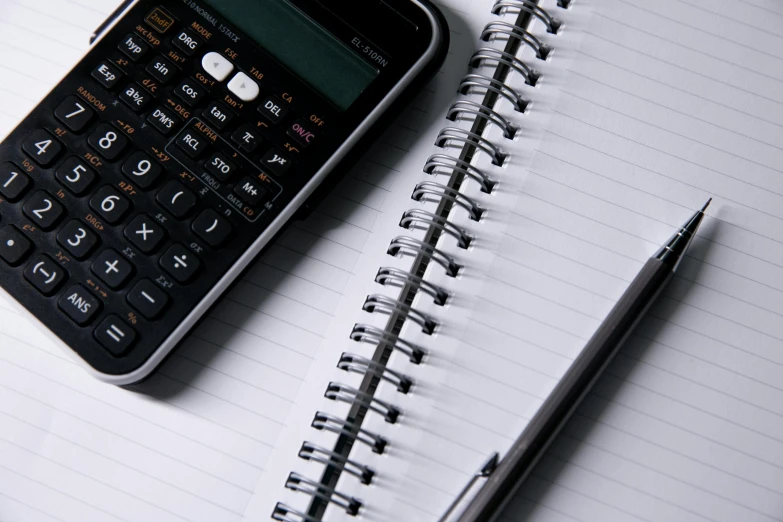 an open notebook, calculator and pen sitting on a table