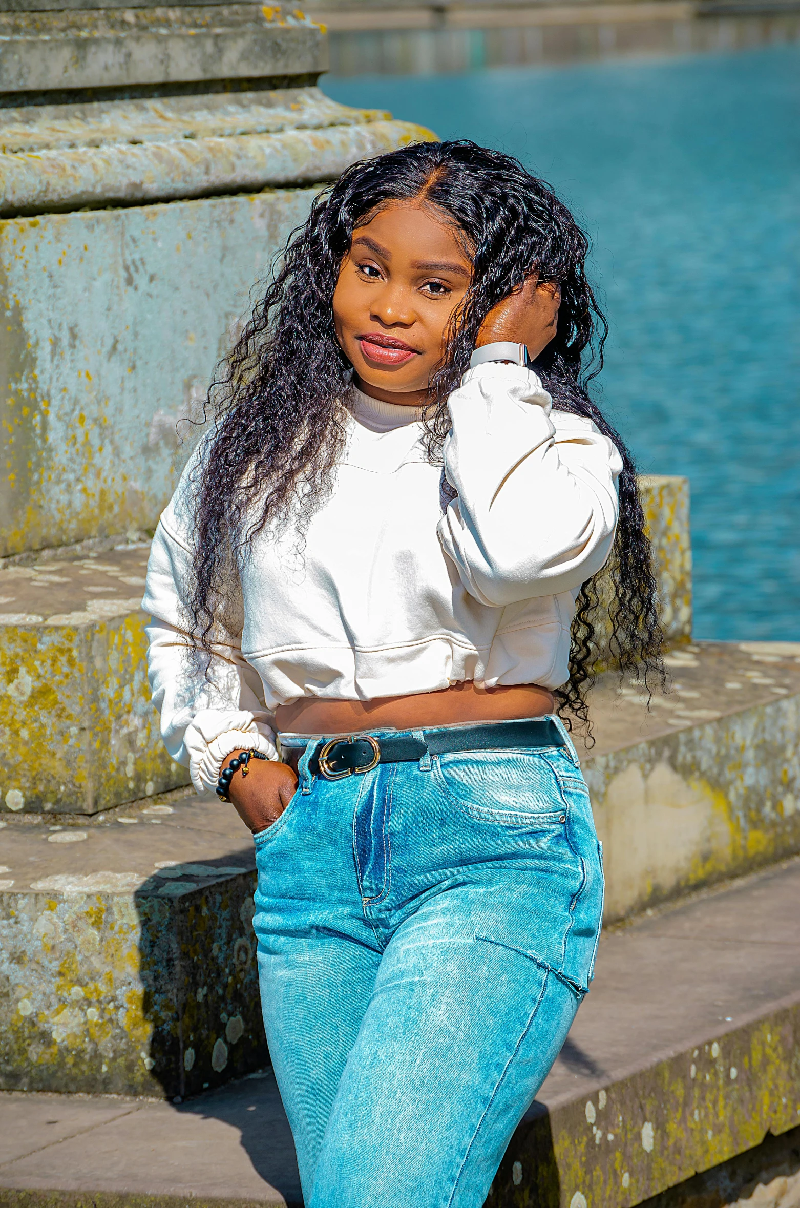 a woman in high rise jeans leaning up against some steps by the water