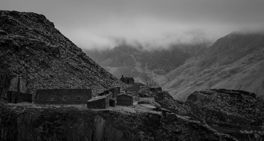 an old house near a cliff and mountains in the fog