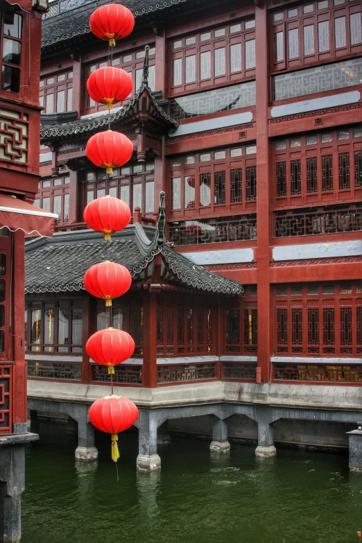 several red lanterns hanging from a roof over a body of water