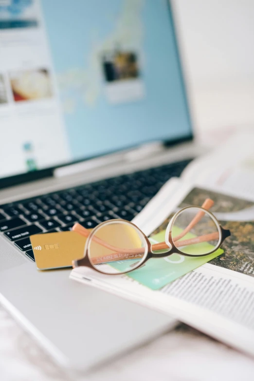 a laptop on a desk with newspaper, magnifying glasses and a book