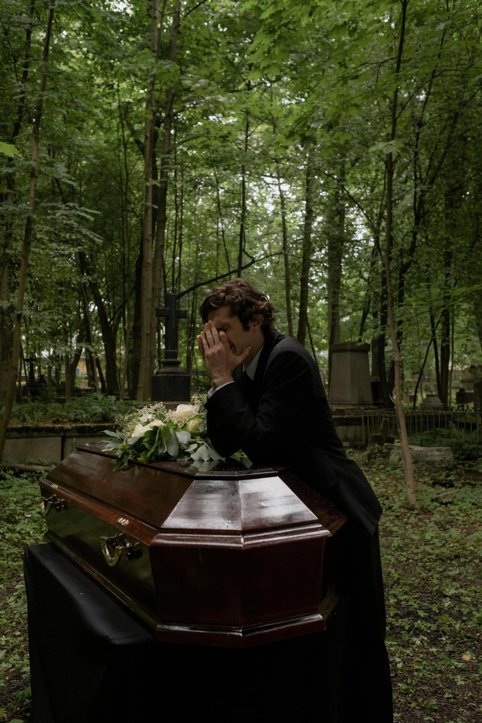 a man in black suit sitting at the edge of a grave