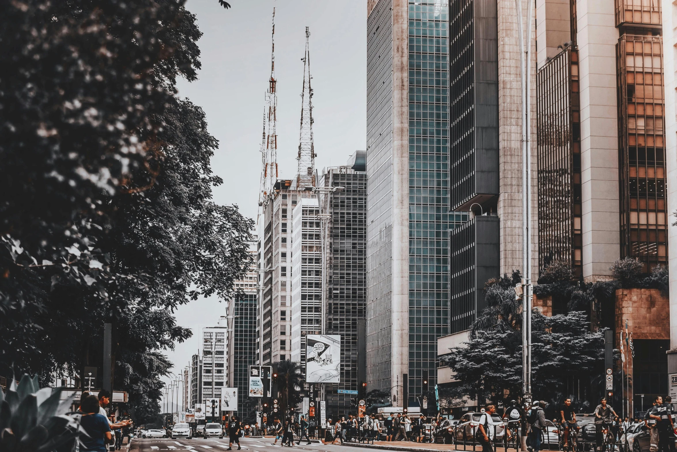 the city view has tall buildings, green trees, and people walking