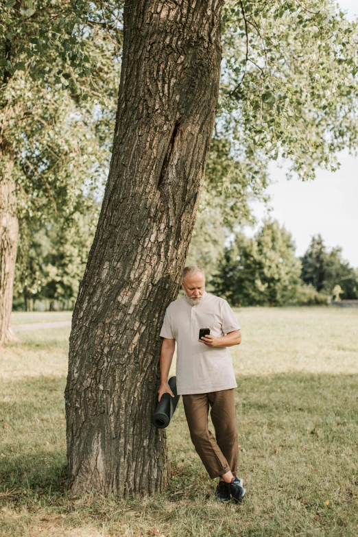 man leaning against tree holding his cell phone