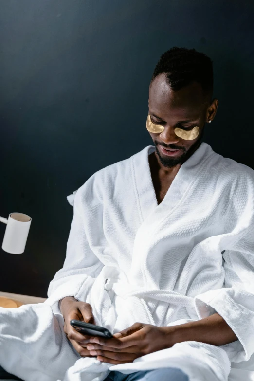 a black man wearing glasses uses a cell phone while sitting in bed