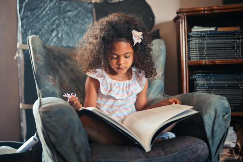 a little girl sitting on a chair reading a book