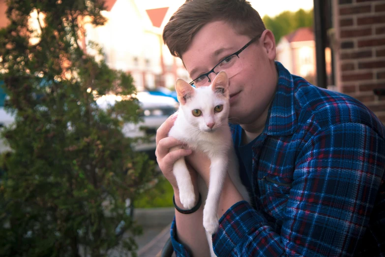 a man is holding a white cat outside