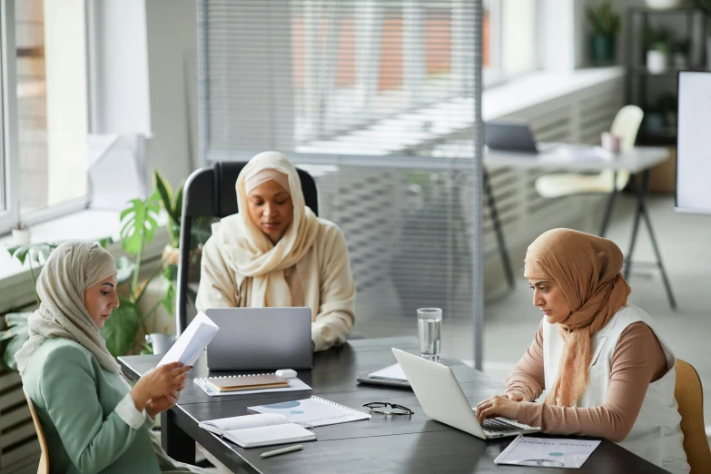 two women sit at a conference table as another looks at papers