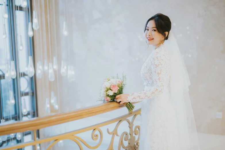 an asian woman in her wedding gown and bouquet smiles as she stands on a staircase railing