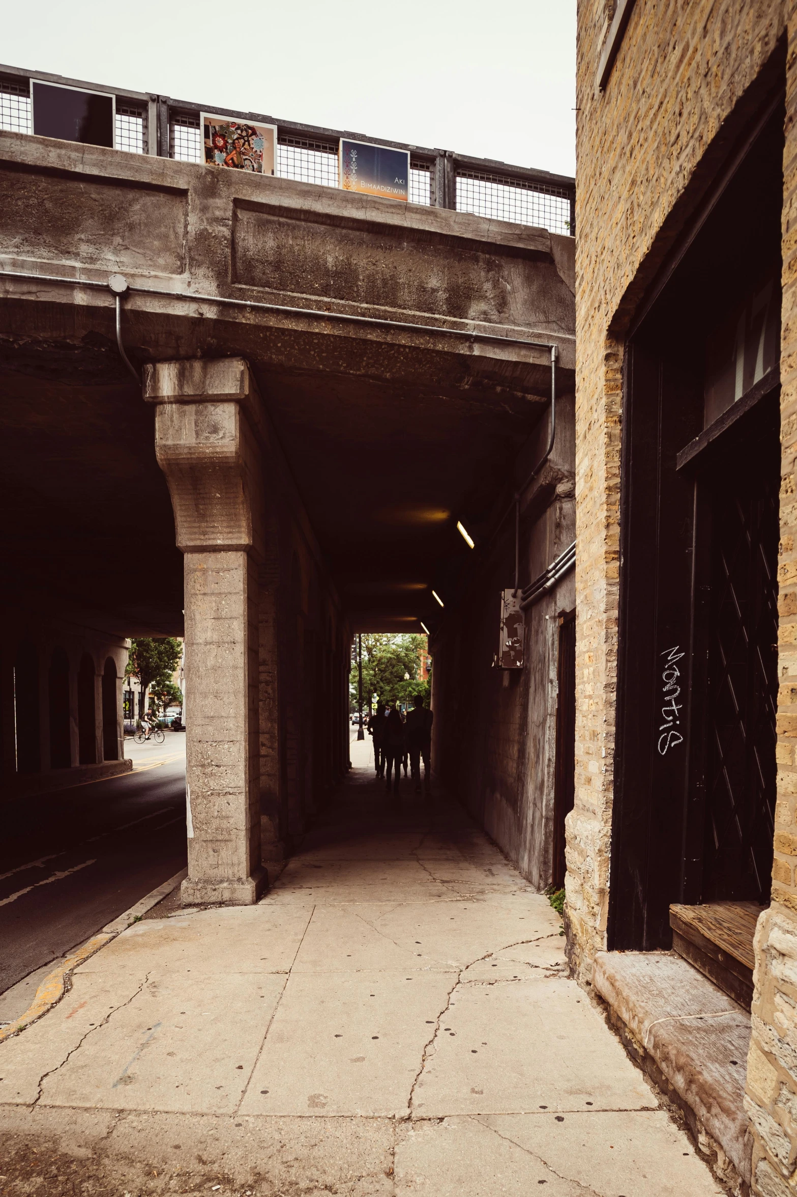 two people standing in an alley beneath a bridge