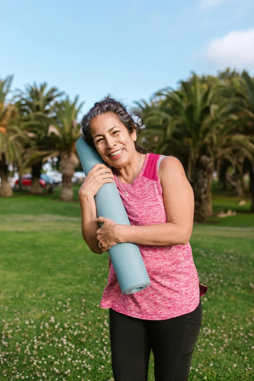 a woman standing in a field holding a long yoga mat