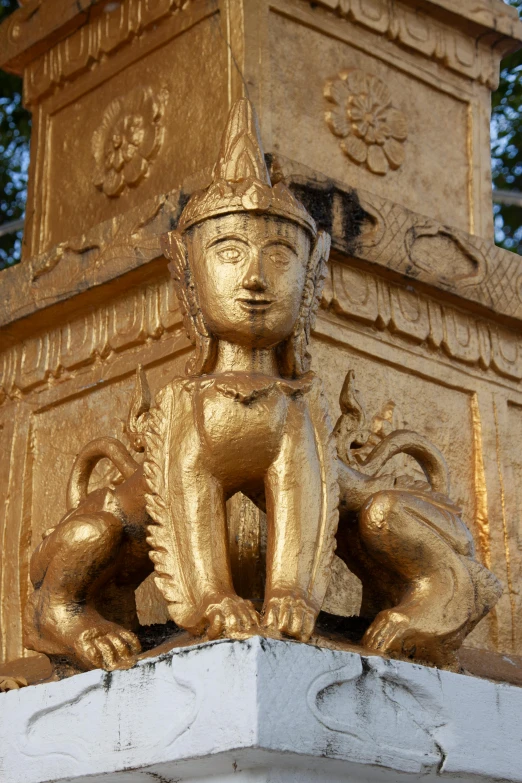 gold statues on top of a gold pillar with trees in the background