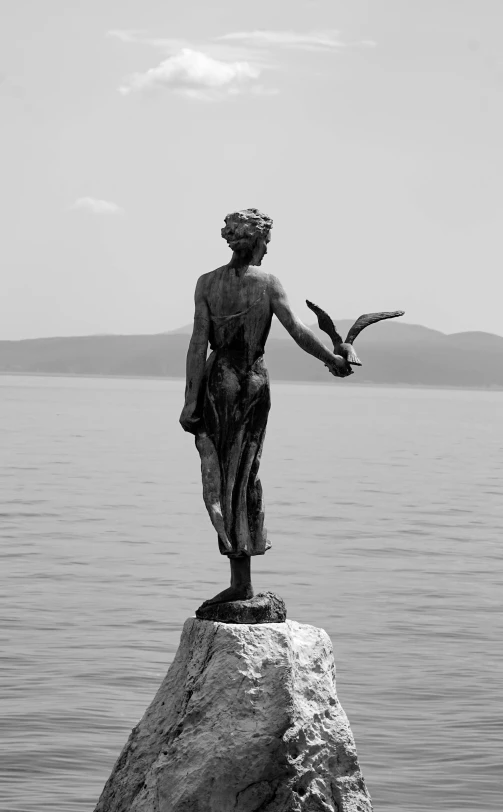 the statue on a rocky outcroppe is holding a bird