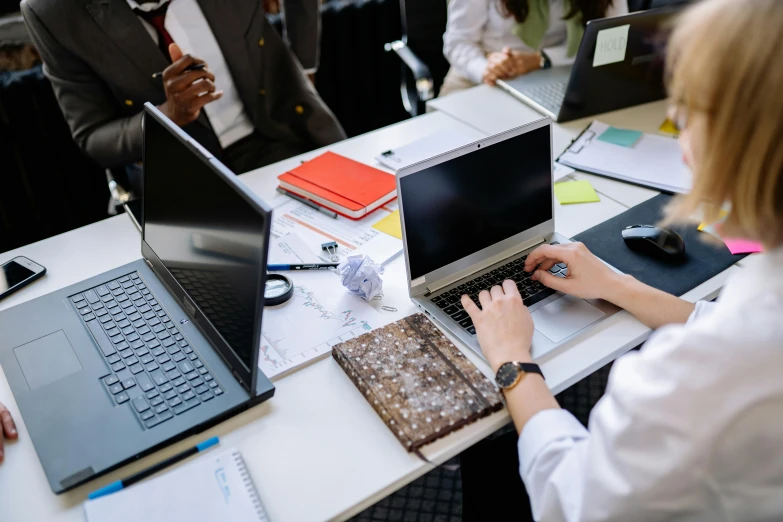 a woman typing on a laptop next to some other laptops