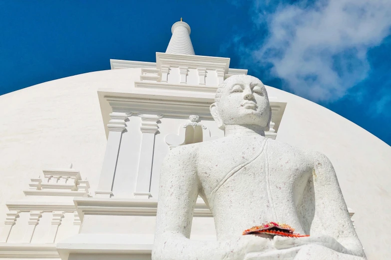 a big buddha statue with a white building and clouds in the background