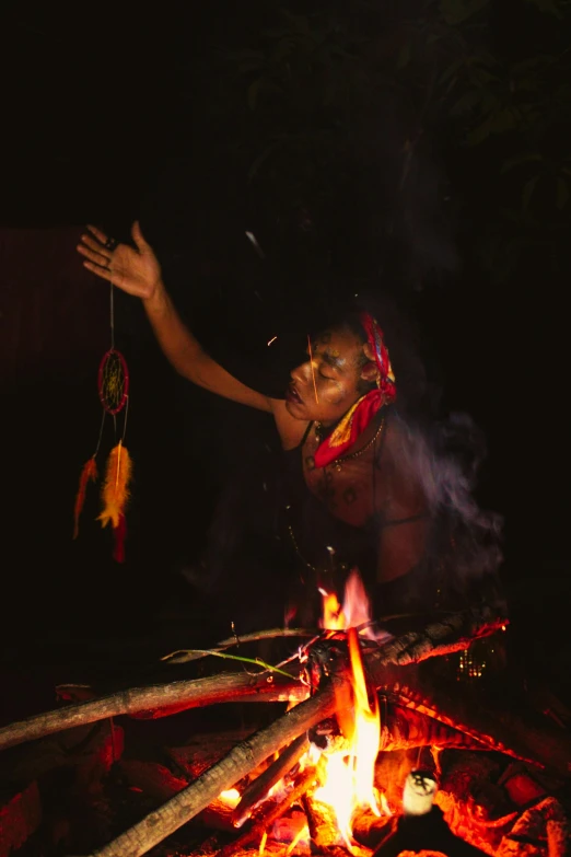 a woman reaching up toward the top of a fire with feathers hanging from it