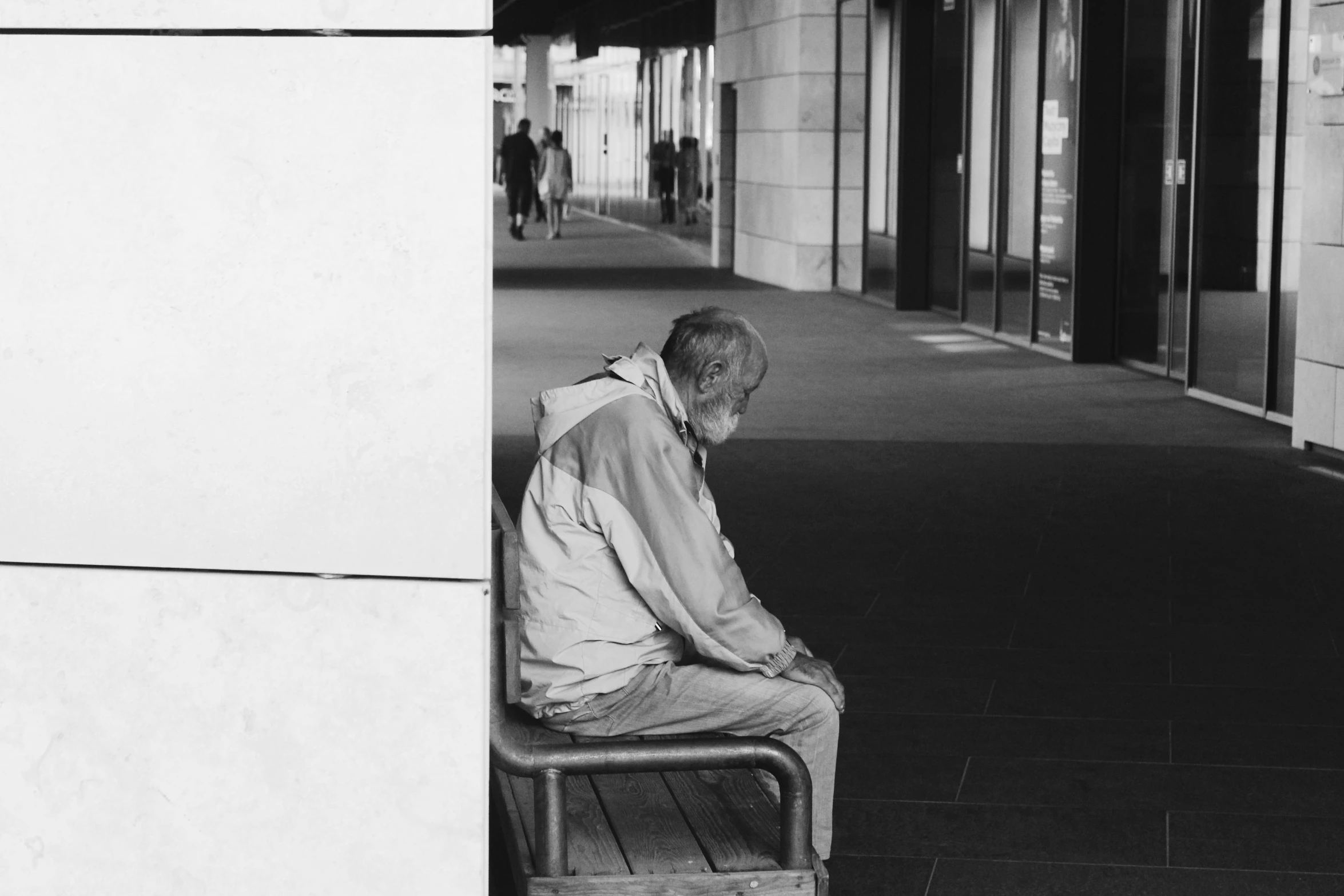 man sitting on a chair in a sidewalk corner next to two large windows