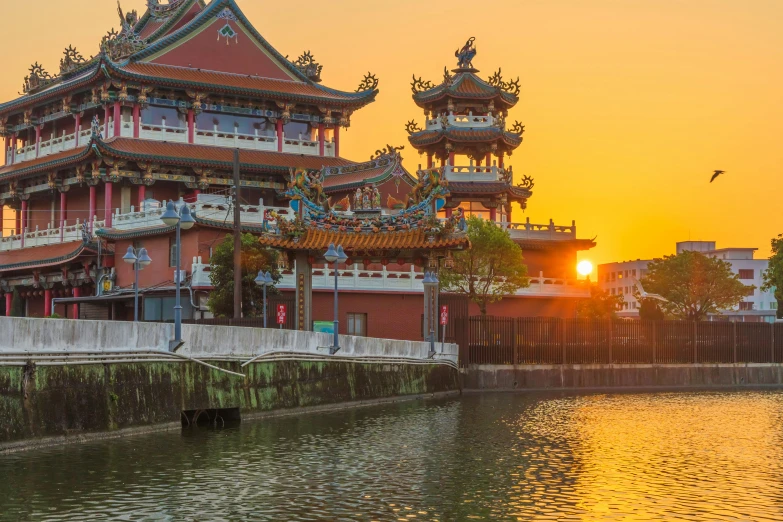 the sun is setting on a chinese structure near water