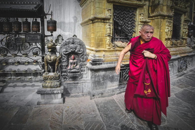 a monk in red dress in front of a large gold building