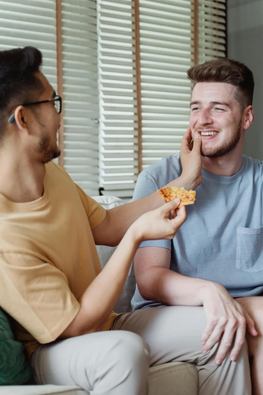 the man is eating pizza and smiling at another man