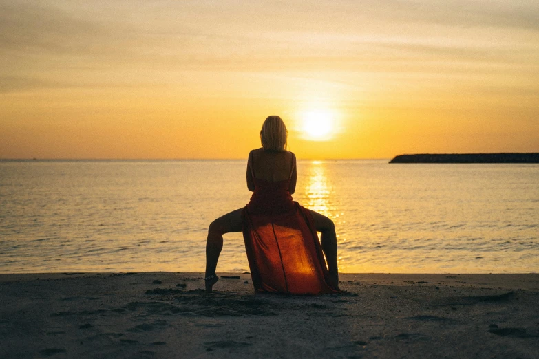 a woman sitting on a beach next to a body of water