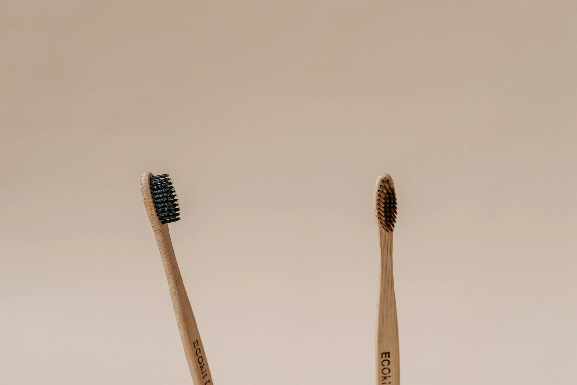 two bamboo toothbrushes with black bristles next to each other