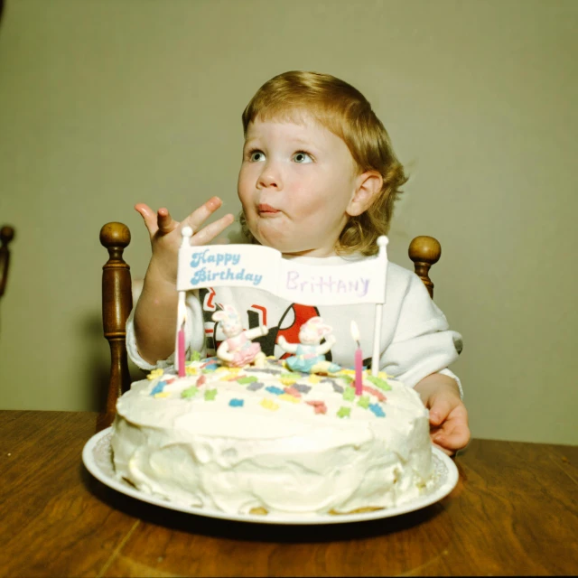 a little girl holding a birthday candle and looking at the cake