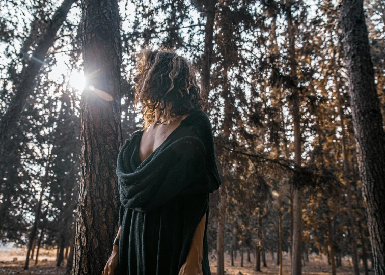 a woman wearing a robe stands in a park with trees