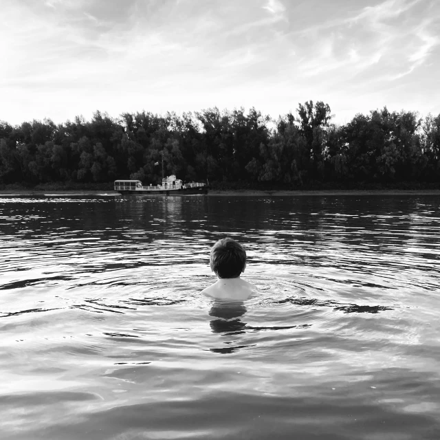 the person is floating in the lake and looking at the boat