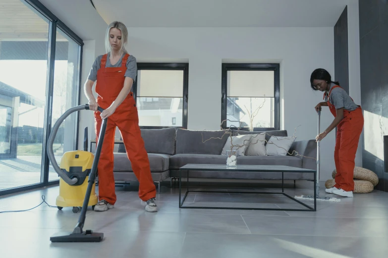 two women are in the living room with vacuums and cleaners