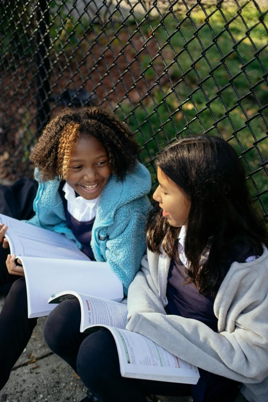 two girls sit on the ground while talking to each other