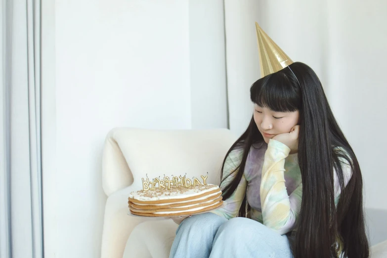 a girl with long hair sitting down next to a cake