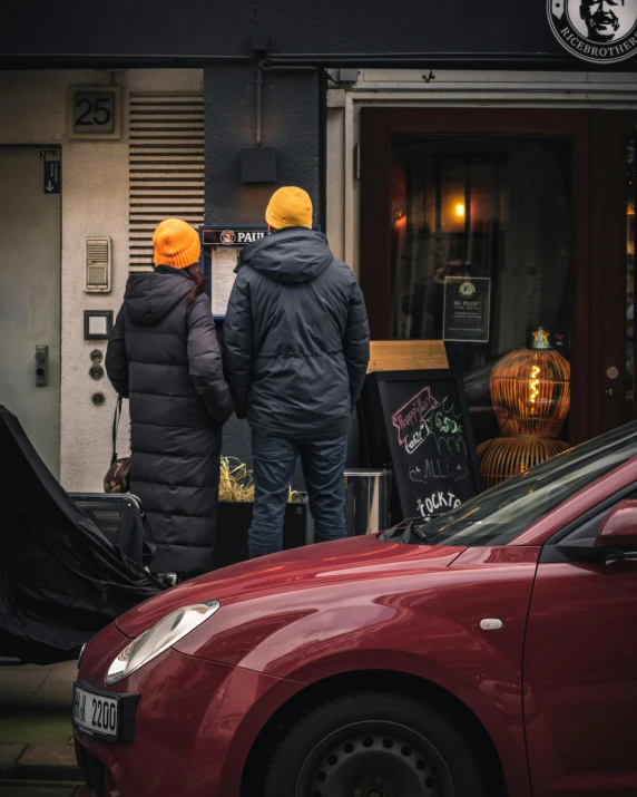 two people outside of a building in front of a car