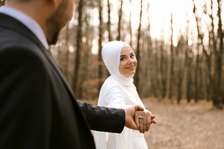 a couple holding hands while standing in a wooded area