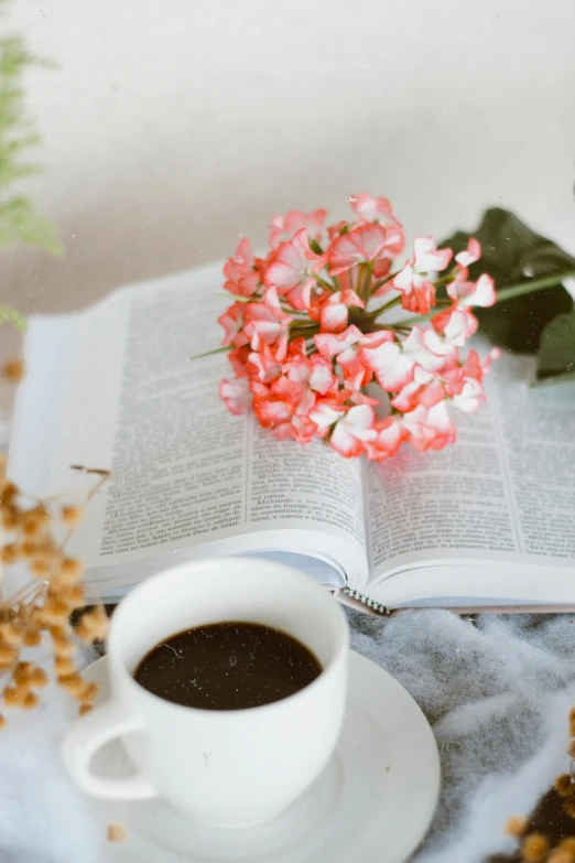 coffee, flowers and an open book on a white table