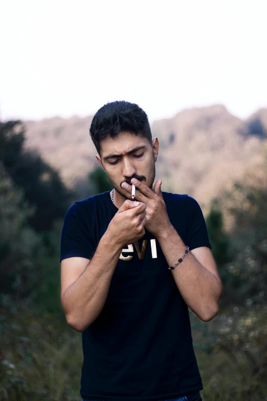 man in black shirt smoking a cigarette with hills in the background