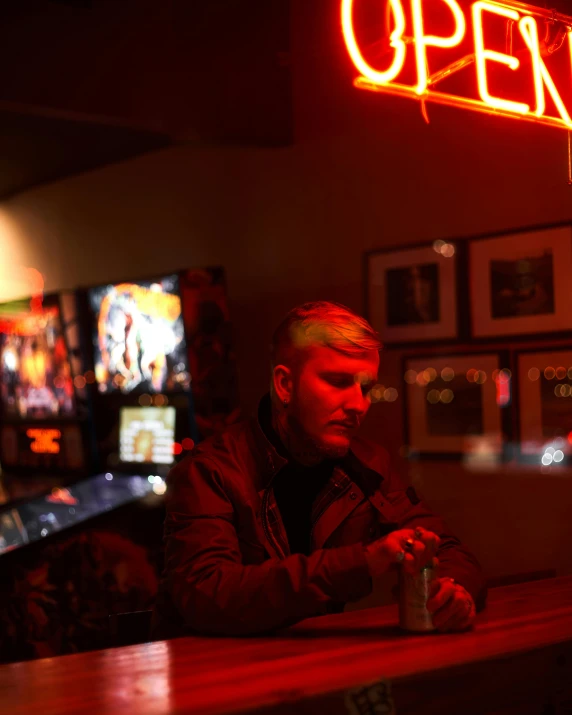 a man sits at a bar with a neon sign above him
