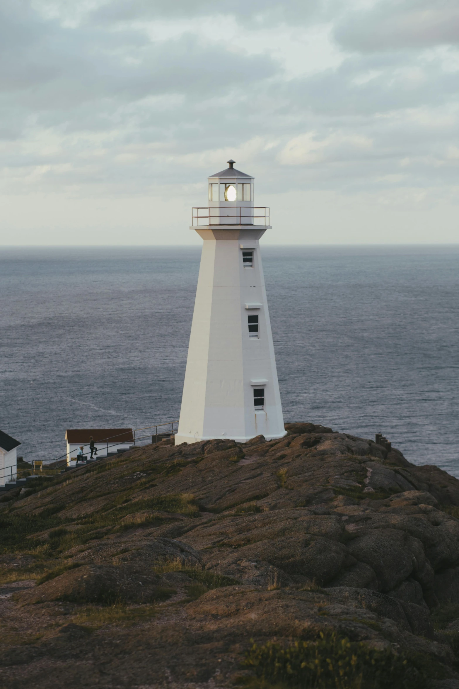 a white light house sitting on top of a rock near the ocean